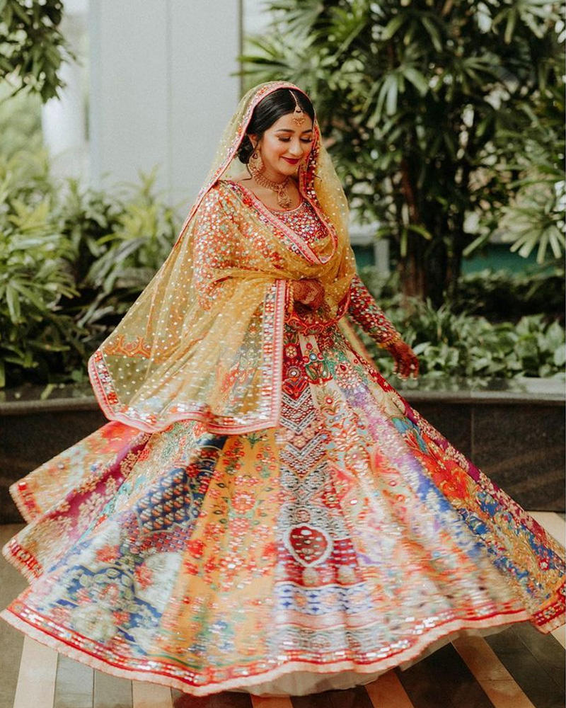 Picture of Medha wears one of our favourite lehnga cholis with perfect grace for her mehndi! A mirrorwork border on the dupatta compliments her vibrant look and the multi panelled lehnga perfectly.